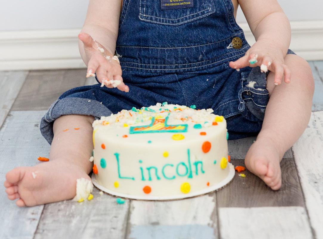 Photo of baby boy from waist down with his birthday cake in front of him between  his legs