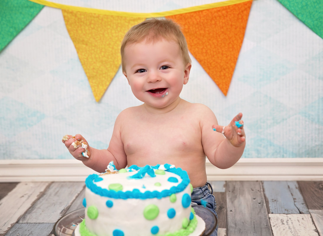 Happy smiling baby sitting in front of a birthday cake one year birthday party photo session