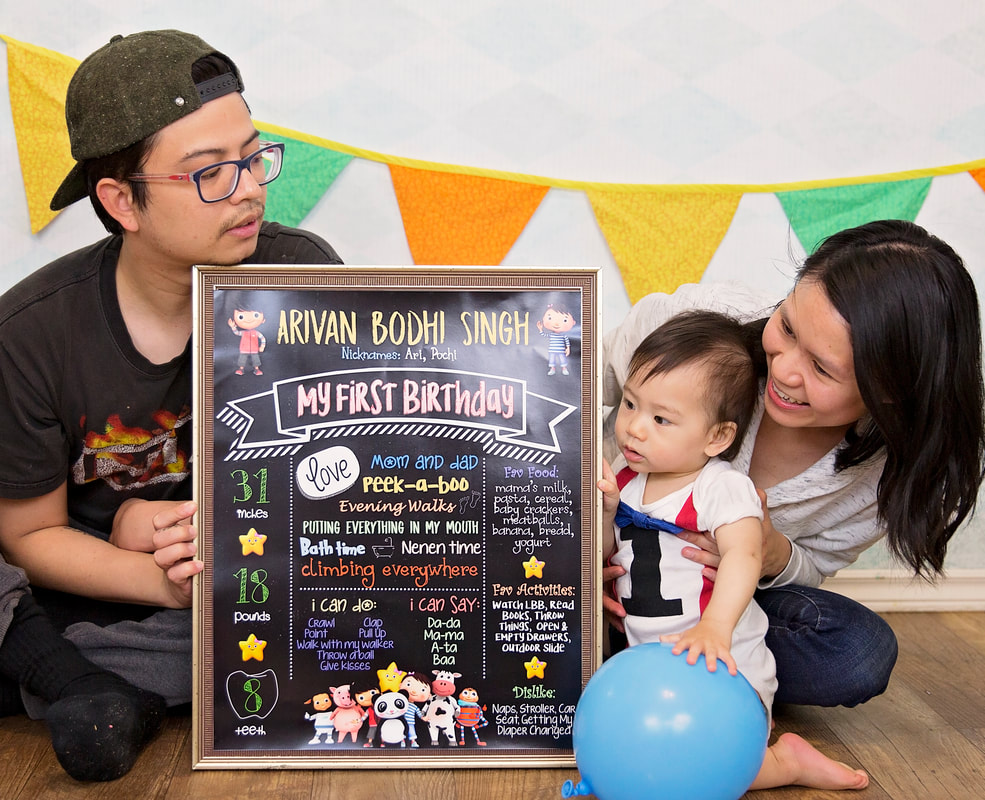 Mom and dad sitting on floor during baby's one year cake smash photo session holding a sign