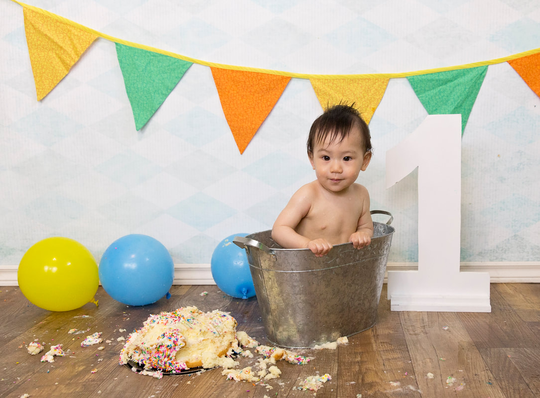 Picture of a baby boy in a small tin bath with smashed cake and balloons all around him first birthday cakesmash photos