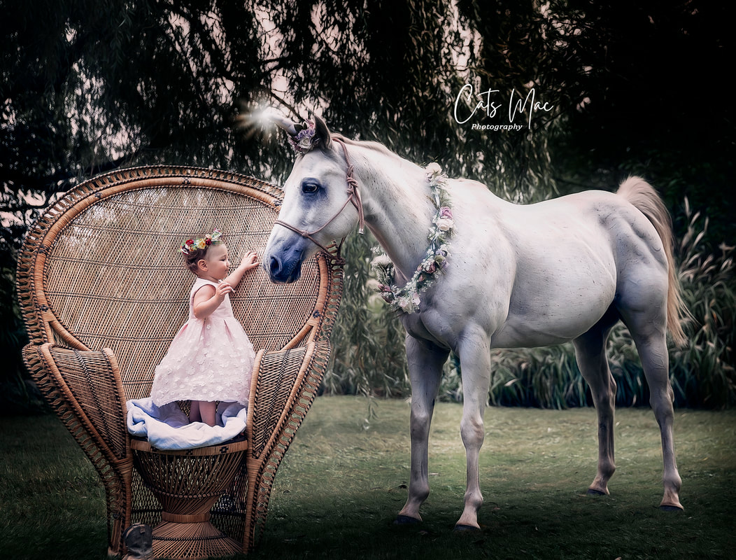 Baby girl standing on a peacock chair looking at a unicorn