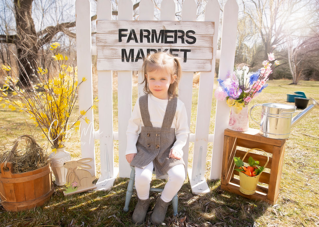 Girl outside sitting in front of a white fence posing for a farmer's market photo session 
