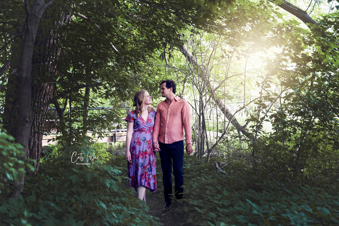 Engagement photo shoot couple walking in forest with sun flare behind them