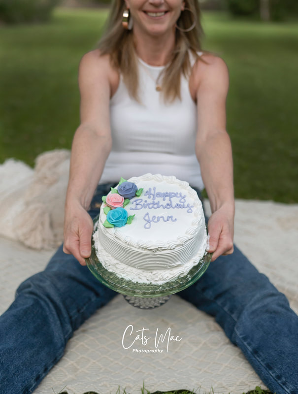 woman holding birthday cake sitting on blanket on ground birthday photo shoot and cake smash