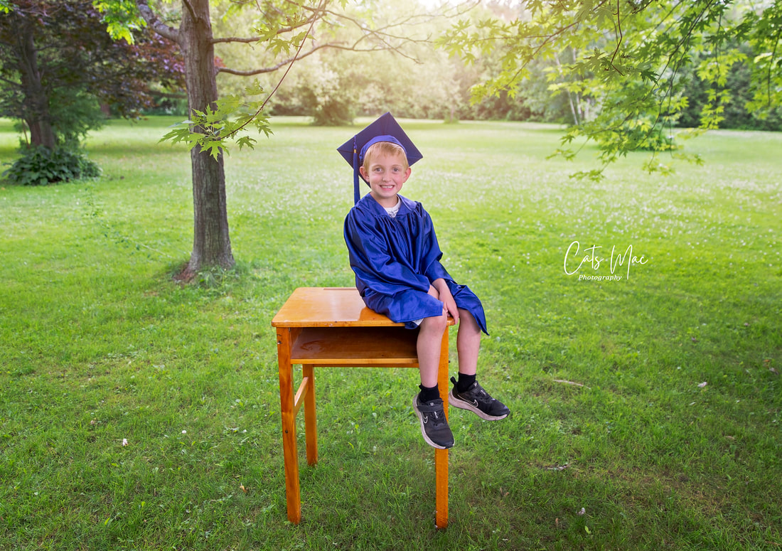 Little boy in graduation cap and gown outside photo session sitting on vintage school desk