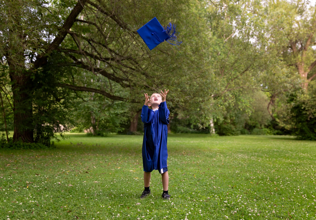 Photo session picture of kindergarten grad outside in cap and gown throwing up cap in air
