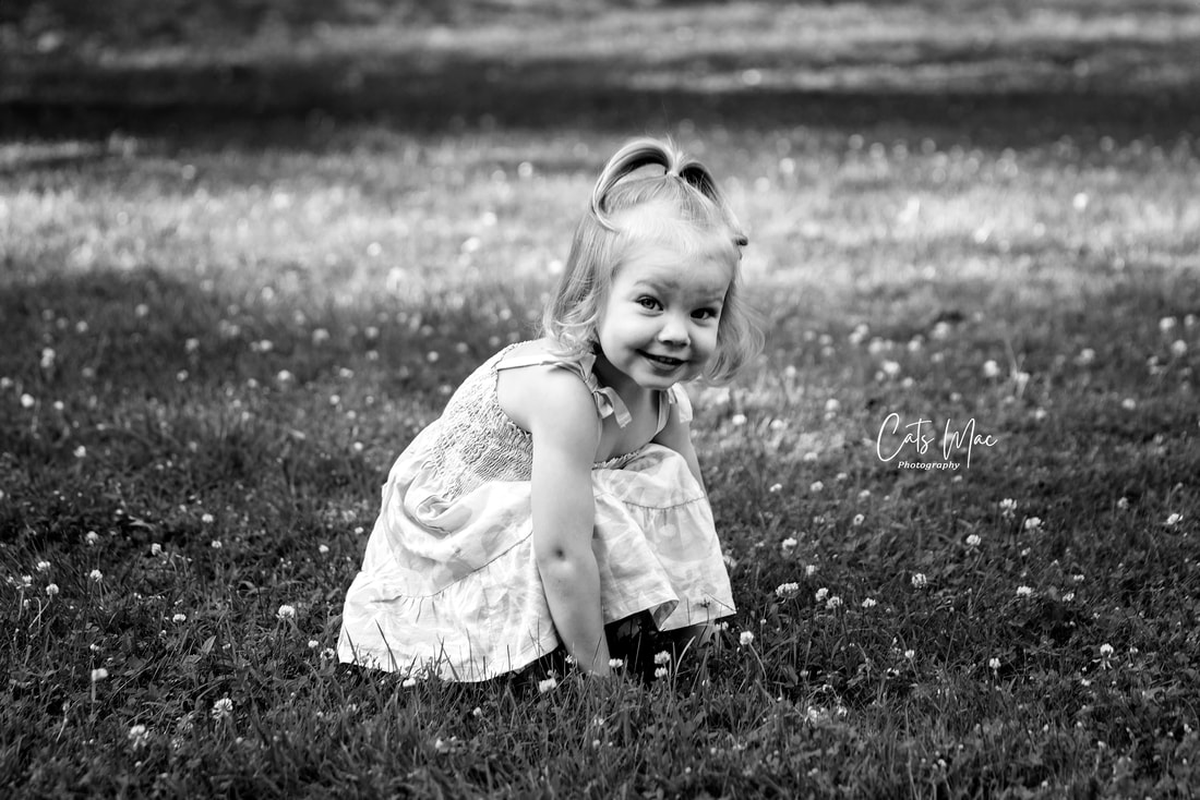 Outside black and white photo of a little girl bending down amount clover