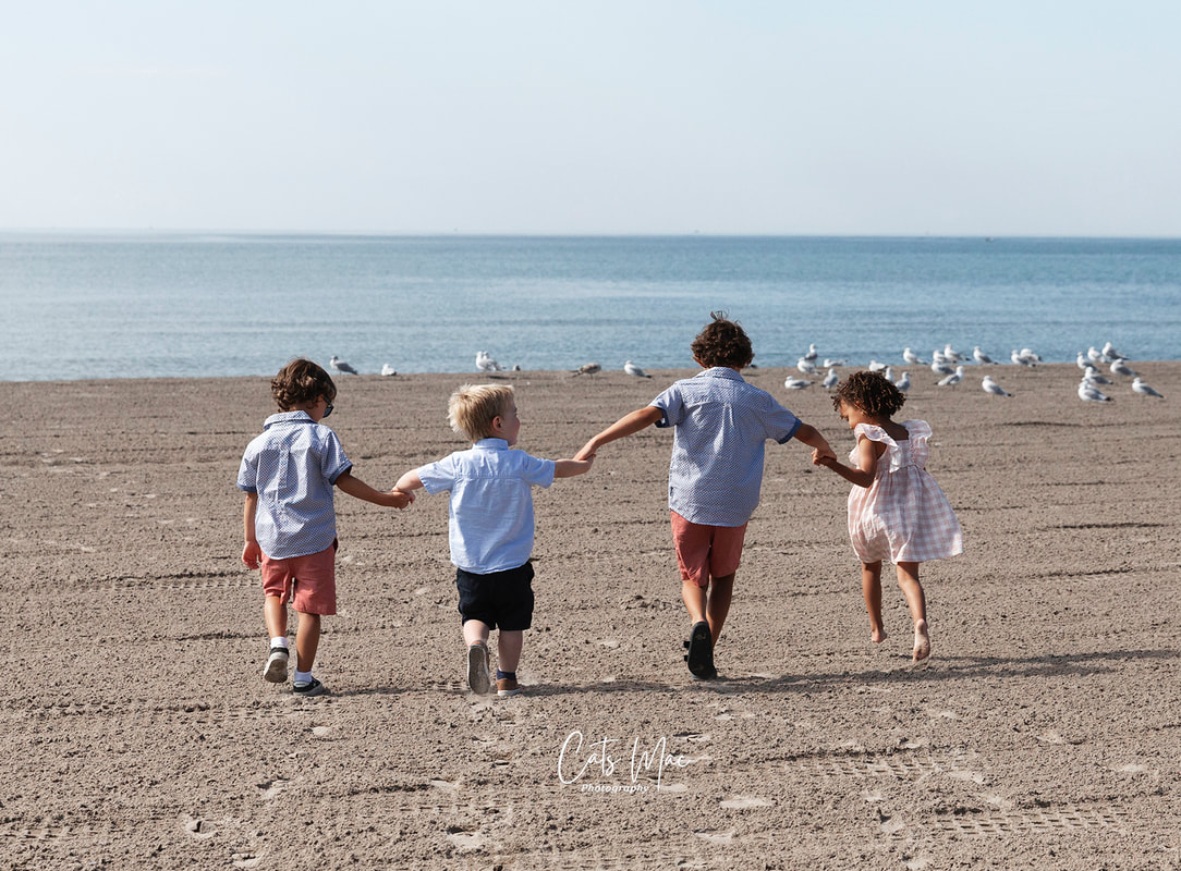 Four young kids holding hands running on the sand towards a bunch of seagulls 