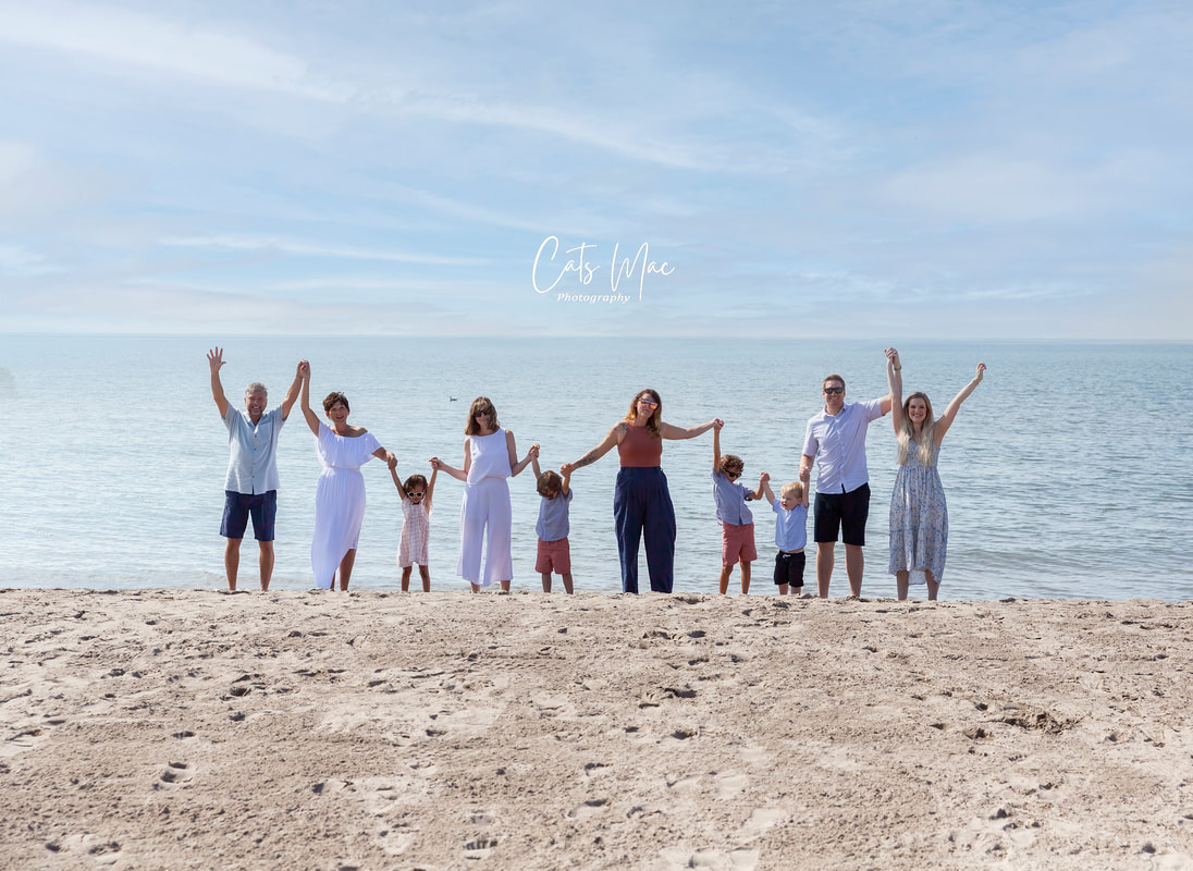 Large family consisting of grandparents, kids and grandkids at beach with arms in the air