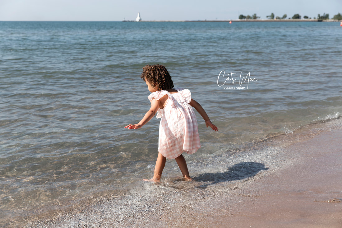 Young girl in white gingham dress dipping her bare feet into water at Cobourg Beach 