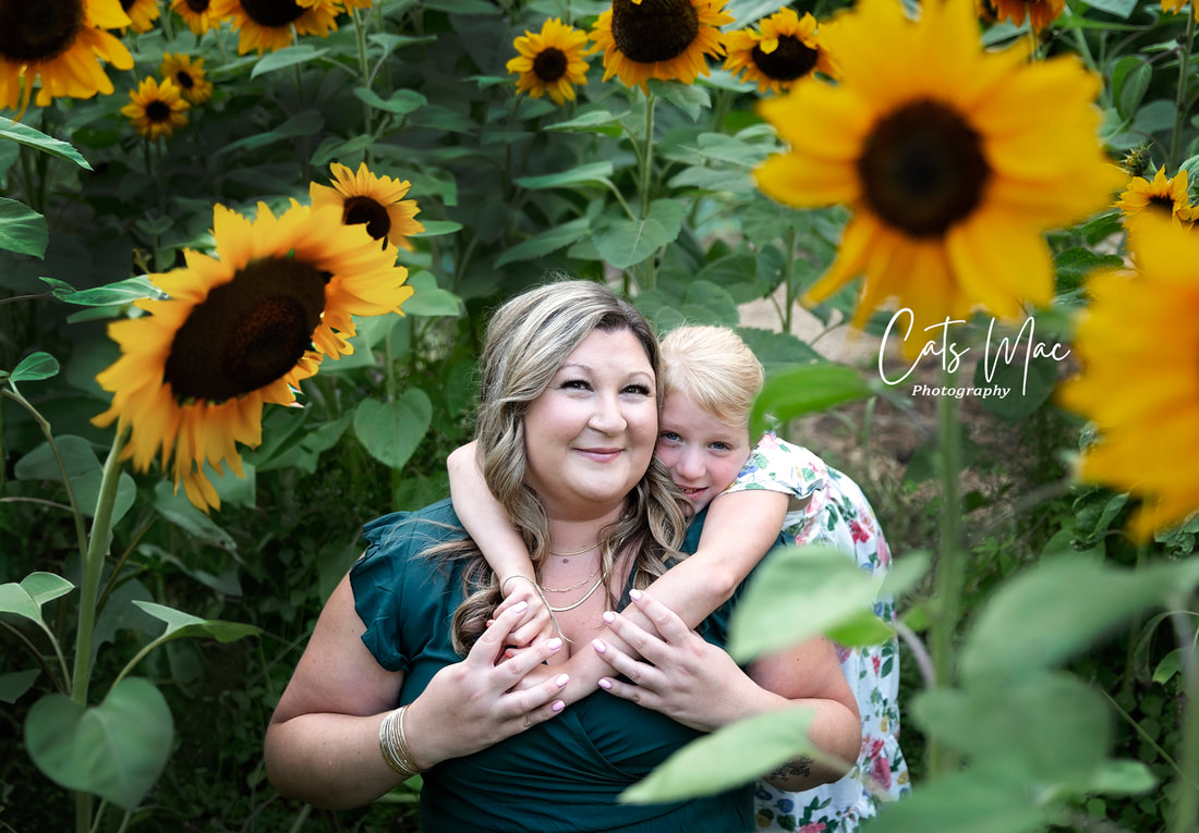 daughter on her mother's back with her arms wrapped around her mother's neck in a field of sunflower patch photo session