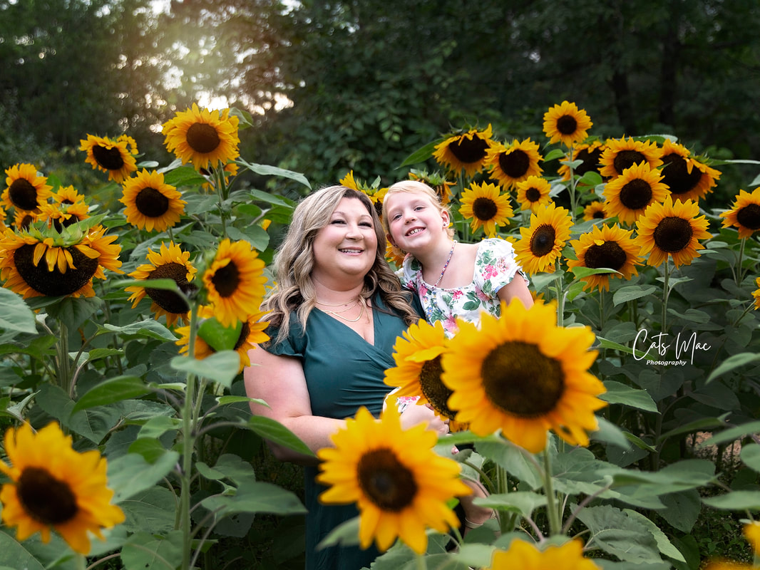 Mother and daughter looking out among a patch of sunflowers in a field photo session 