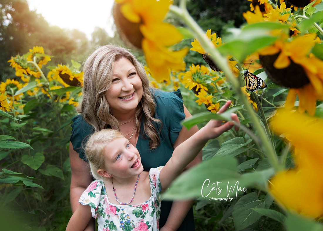 Little girl pointing towards a monarch butterfly with a patch of sunflowers with her mother looking on