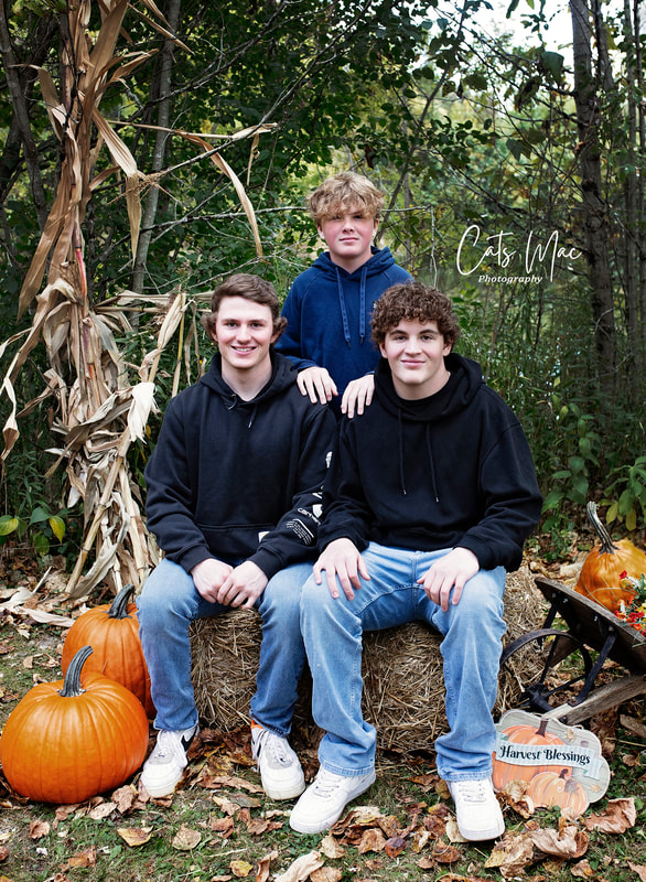 Fall family photo shoot teenage brothers sitting on hay bales with pumpkins