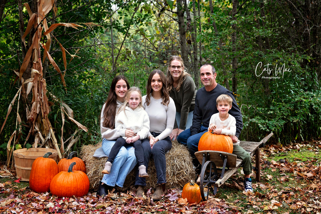 large family photo session sitting on bales of straw among fall leaves and pumpkins