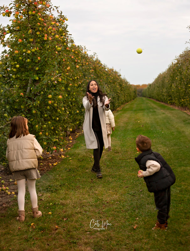 Adult and two kids catching an apple between them fall family photo shoot apple orchard