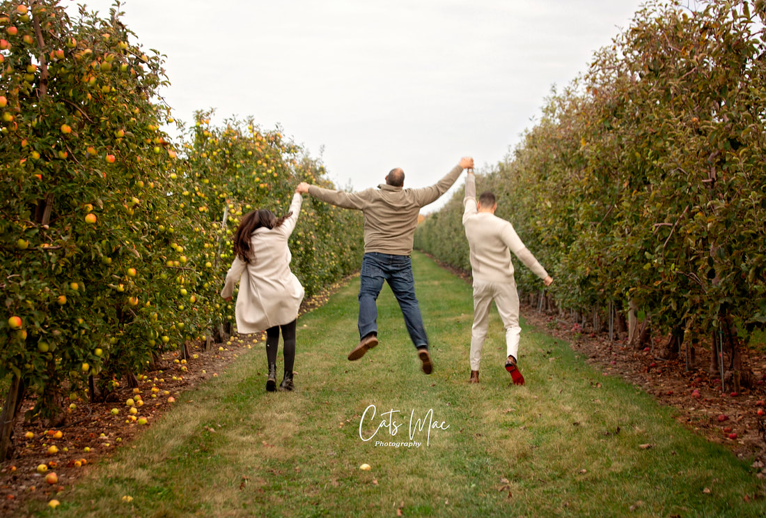 Three adults jumping in air walking down apple tree aisle