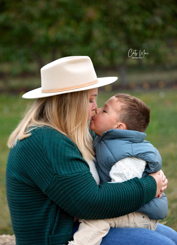 Mom with white cowboy hat on kissing little boy apple orchard