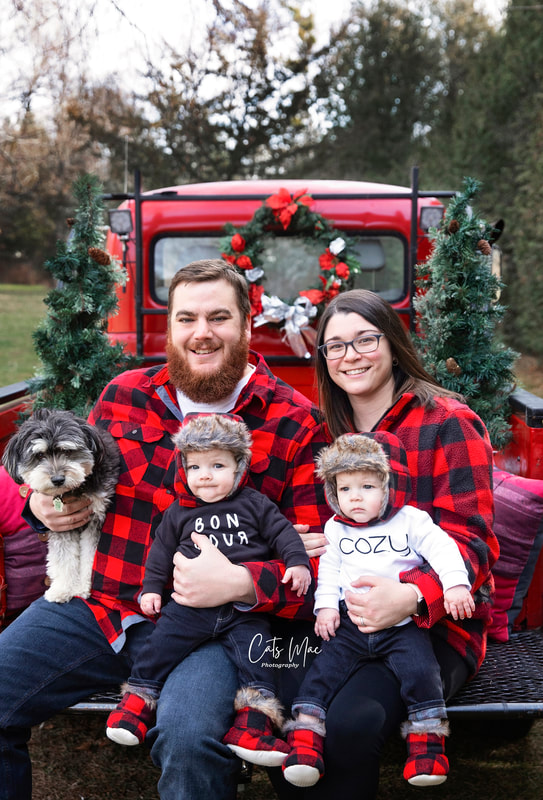 family dressed in red with twin boys and dog sitting in back of vintage red truck for Christmas Photo session