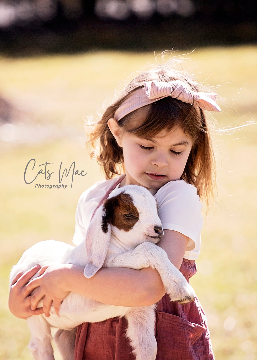 Girl holding a baby goat in her arms and looking down at the goat's eyes