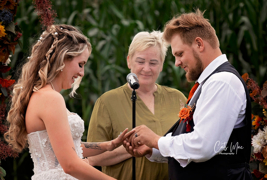 Bride and groom exchanging rings in front of officiant in front of cornfield