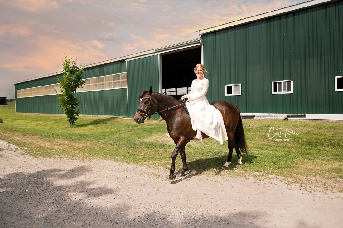 Bride in wedding gown riding horse away from green stables