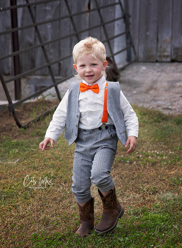 Boy toddler in orange bow tie with orange suspenders and grey suit at wedding ring bearer