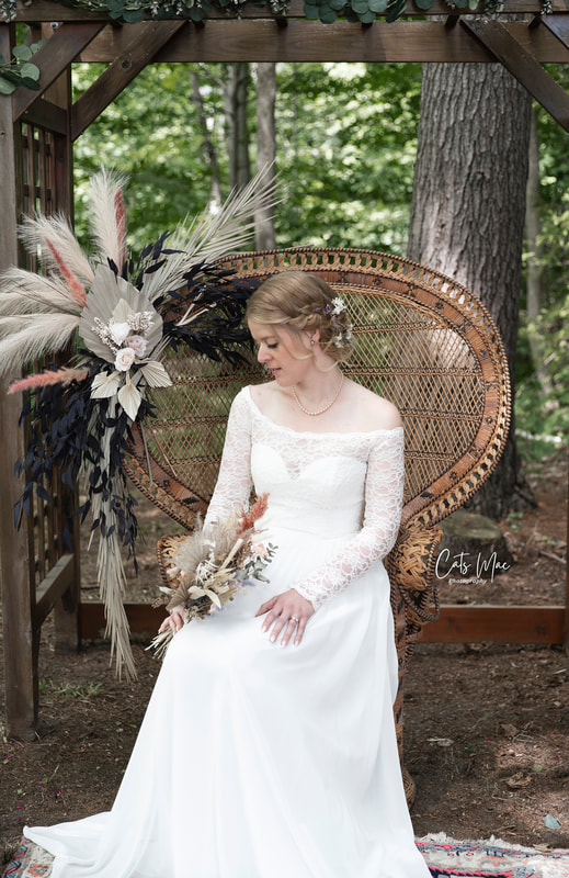 Bride sitting on a bohemian decorated vintage peacock chair looking down at her bouquet