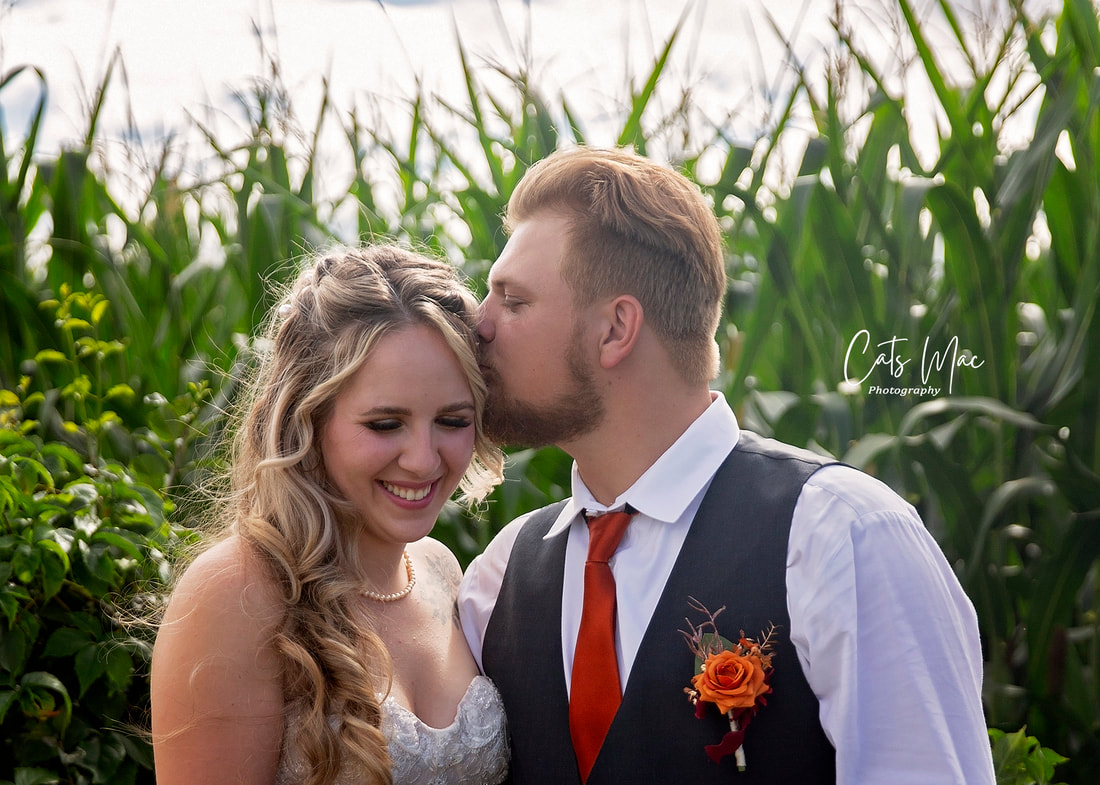 Groom kissing temple of bride outside corn field
