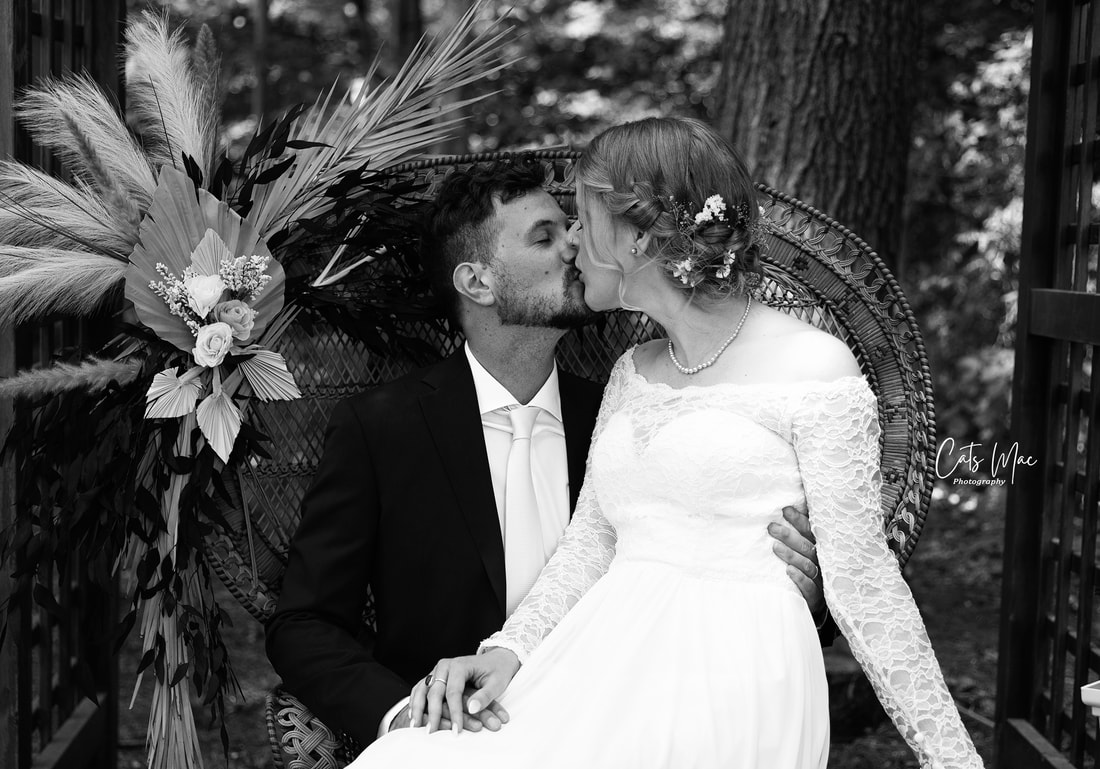 Black and white photo of a bride and groom sitting on a vintage peacock chair kissing