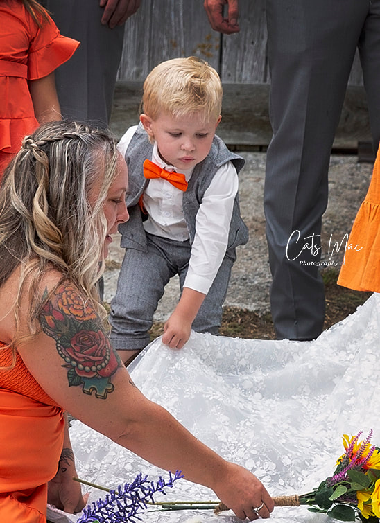 Little boy ring bearer helping arrange bride's dress