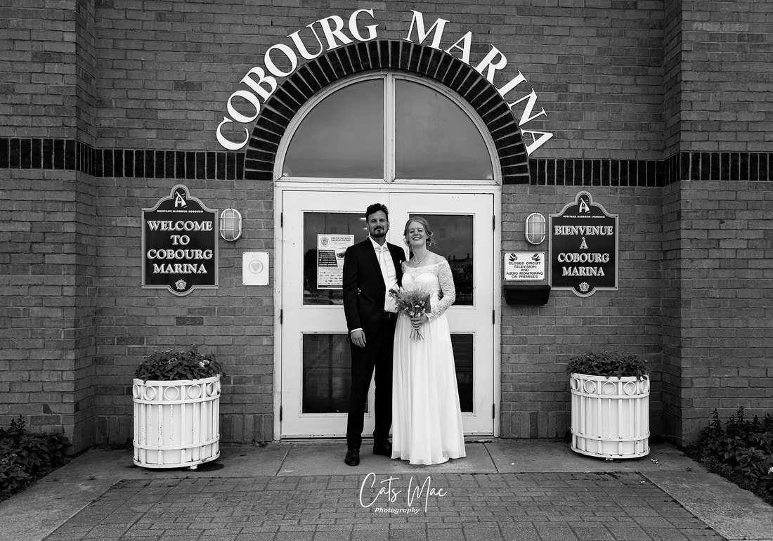 black and white photo of a bride and groom standing in front of the doors of Cobourg Marina